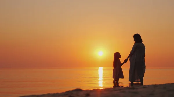 Uma mulher grávida com uma filha está de pé na praia ao pôr do sol. À espera do segundo filho — Fotografia de Stock