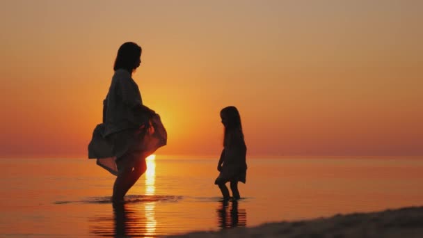 Gravid kvinna med sin dotter ha kul på stranden, stänk vatten på varandra — Stockvideo