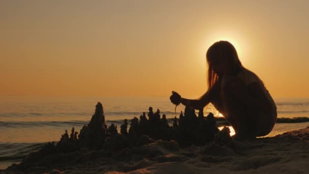 一个孩子的剪影, 在海滩上建造一个沙子城堡, 一个美丽的日落 — 图库视频影像