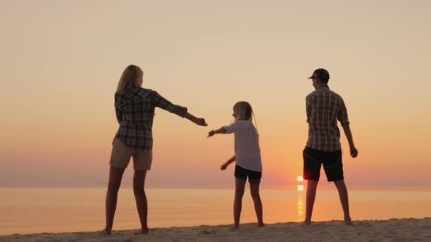 Una madre joven con dos hijos está enseñando un movimiento de baile de moda. En la playa al atardecer. Concepto de Comunión de Generaciones — Vídeo de stock