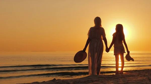 Uma mulher segura uma mão de criança, junta-se à beira-mar, olha para um lindo pôr-do-sol. Mãe com filha — Fotografia de Stock