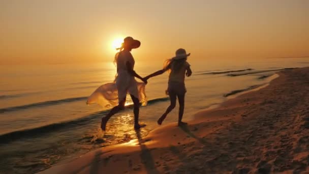 子どもを持つ女性は、海で水の縁に沿ってうっかり実行されます。美しい夕日 — ストック動画