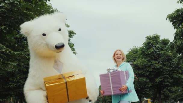 A bright young girl and a polar toy bear are having fun holding colorful gifts in wrapping paper, smiling at the camera — Stock Video