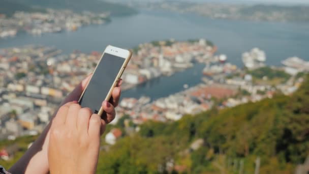 Manos femeninas con un smartphone. Utilice el teléfono contra el fondo de la ciudad de Bergen — Vídeos de Stock