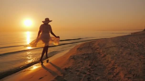 Una donna in una coppia leggera cammina lungo la spiaggia al tramonto. Donna spensierata e allegra — Video Stock