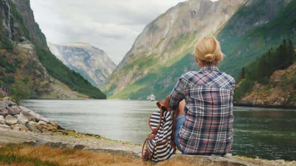 Una mujer se sienta en la orilla de un pintoresco fiordo en Noruega, admira la hermosa vista del fiordo Neroy, una rama del fiordo Sognefjord. Turismo en Escandinavia — Vídeos de Stock