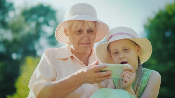 Het meisje speelt op de smartphone, de grootmoeder is naast haar zitten en kijken naar haar — Stockvideo