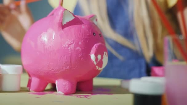 As crianças em conjunto pintam um banco piggy no rosa. Jogos com conceito de crianças — Vídeo de Stock