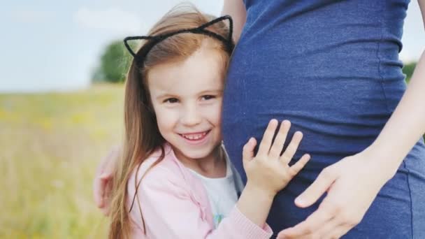 Retrato de uma menina bonita perto da barriga de sua mãe grávida — Vídeo de Stock