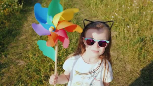 Portret van een stijlvolle klein meisje met een speelgoed windmolen in haar handen — Stockvideo