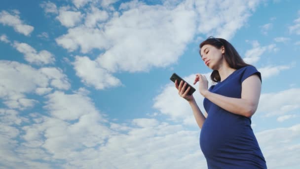 Mujer embarazada tomando una foto contra el cielo azul — Vídeos de Stock