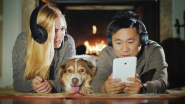 Genç bir çift bir tablet şömine yakın kullanıyor. Onları yanında onların köpek yatıyor. Teknoloji ve konfor ev kavramı