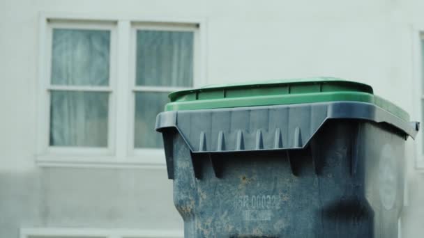 Мужчина бросает мешок мусора в мусорное ведро возле своего дома — стоковое видео
