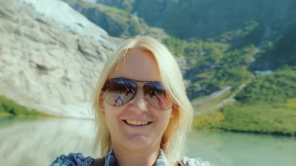 サングラスの女性は、ビデオで自分を撮影します。ノルウェーの氷河と山の背景 — ストック動画