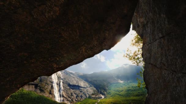 Solen skiner genom ett hål i berget, där du kan se berg med ett vattenfall och en pittoresk dal. Fantastiskt vacker plats, resenärer dröm, inga människor — Stockvideo