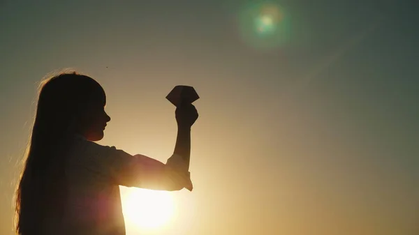 Ανέμελο κοριτσάκι παίζει με ένα αεροπλάνο το χαρτί στο ηλιοβασίλεμα. Όμορφη φακού φωτοβολίδα στο πλαίσιο — Φωτογραφία Αρχείου