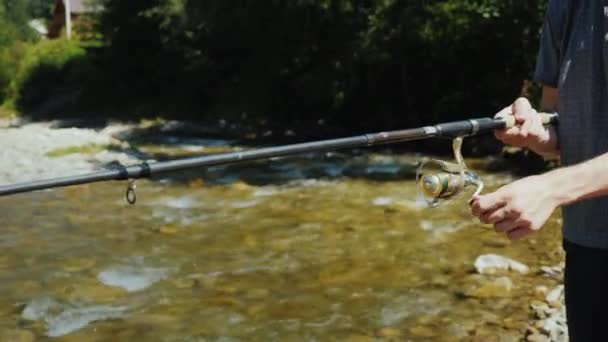 Een jongeman is vissen rond een kleine rivier, een zijaanzicht, alleen de handen zichtbaar in het frame zijn — Stockvideo