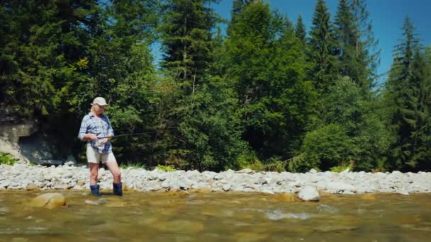 Una joven está pescando cerca de la orilla de un río de montaña. Vacaciones de verano activas en el campo — Vídeos de Stock