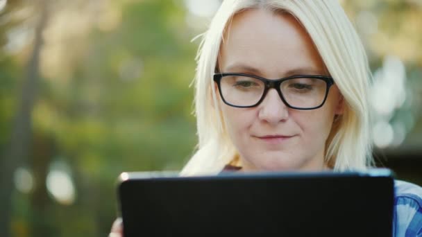 Portret van een jonge vrouw in het park, geniet van een tablet — Stockvideo