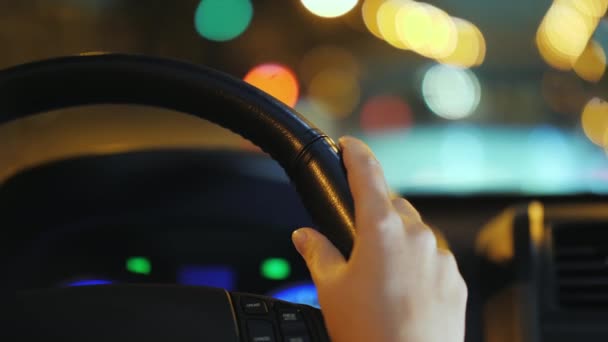 Γυναικεία χέρια στο τιμόνι του αυτοκινήτου. Βόλτες μέσα στην πόλη νύχτα, όμορφη bokeh από το αντίθετο ρεύμα αυτοκίνητα — Αρχείο Βίντεο