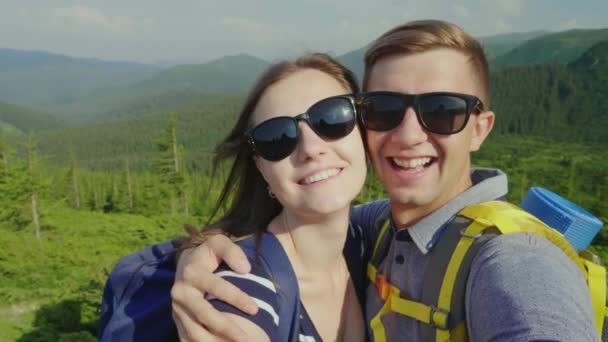 Una feliz pareja de turistas se fotografiaron a sí mismos, sonriendo a la cámara. En el contexto de un pintoresco paisaje de montaña — Vídeos de Stock