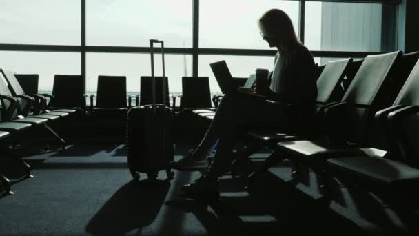 Femme d'affaires attendant son vol à l'aéroport international. Elle boit du café, utilise un ordinateur portable — Video