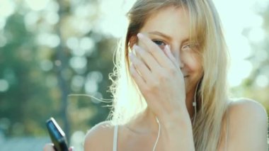 Kulaklığımda mutlu kadın müzik dinliyor, bir akıllı telefon kullanır. Güneş güzel saçlarını aydınlatır