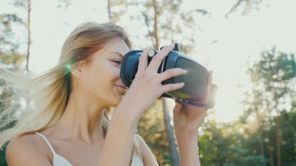Погрузиться в виртуальную реальность. Молодая женщина надевает шлем виртуальной реальности на солнце. Ветер стучит по ее волосам — стоковое видео