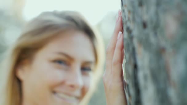 Счастливая молодая женщина стоит возле дерева, портрет. Смотрит в камеру, улыбается . — стоковое видео