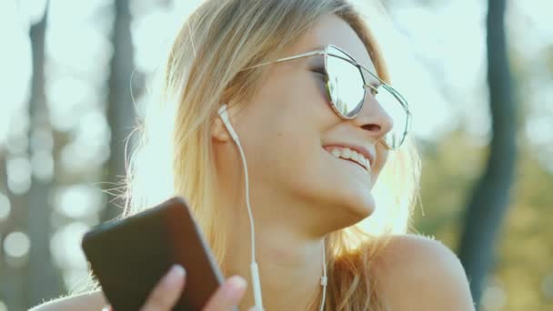 Aantrekkelijke jonge vrouw luisteren naar muziek. Portret in de zon — Stockvideo