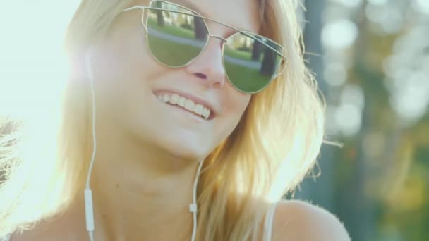 Una mujer de apariencia modelo en gafas de sol. Escucha música bajo el sol — Vídeo de stock