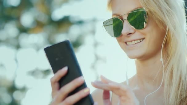 Mutlu bir smartphone kadın güneş gözlüğü kullanın. Tatile, güneş ışınlarının güzel saçlarını aydınlatmak — Stok video
