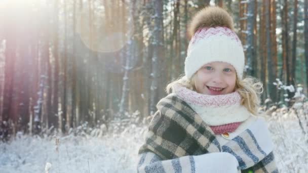 Retrato de una niña feliz envuelta en una tela a cuadros en un bosque de invierno cubierto de nieve — Vídeo de stock