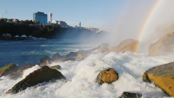 Foten av Niagarafallen. I fjärran kan du se den kanadensiska kusten med byggnader av hotell och underhållning centers för turister — Stockvideo