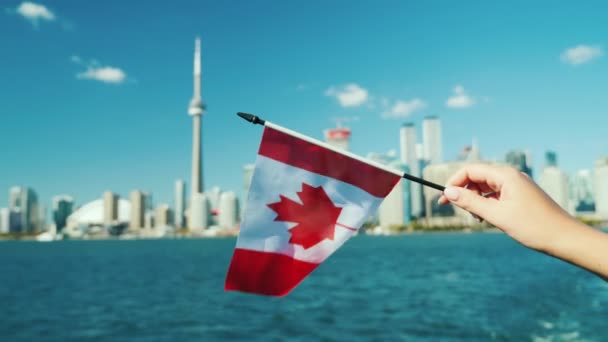 Mano sosteniendo una bandera canadiense en el fondo de la línea de la ciudad de Toronto — Vídeo de stock