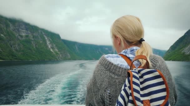 Una mujer se para en la popa de un crucero, mira las rocas en retirada y las olas del fiordo — Vídeo de stock