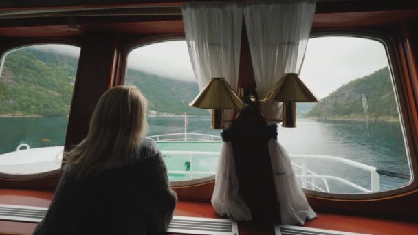 Женщина смотрит из иллюминатора на прекрасный пейзаж Норвегии. Поплавки на корабле на норвежских фьордах — стоковое видео