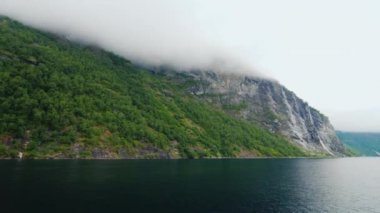 Güzel dağlar, tepeler, sis ve bulutlar gömülüdür. Norveç güzel doğası, bir cruise görünümünden fiyort suları arasında yüzen gemi