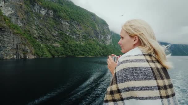 Eine Frau mit einer Tasse Tee in der Hand an Bord eines Kreuzfahrtschiffes. Blick auf die wunderschönen Berge des Fjords — Stockvideo