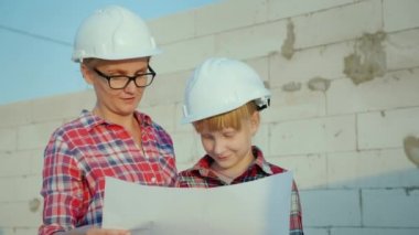 Bir kadın kızıyla birlikte onların gelecekteki ev projesi eğitimi alıyor. Kask inşaat sitede ayakta