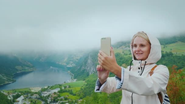 Un turista feliz es fotografiado en el fondo de un pintoresco fiordo en Noruega. Vale la pena en un objeto fotográfico popular - un acantilado volador — Vídeo de stock