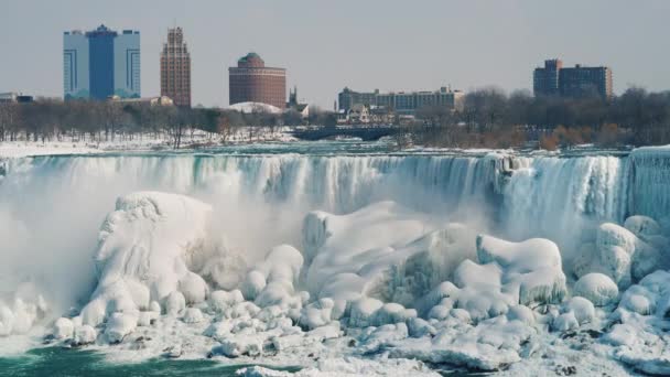 Amerikaanse zijde van Niagara Falls in de winter. De gebouwen van hotels en centra van het vermaak zijn zichtbaar. Water valt op blokken van ijs en sneeuw — Stockvideo