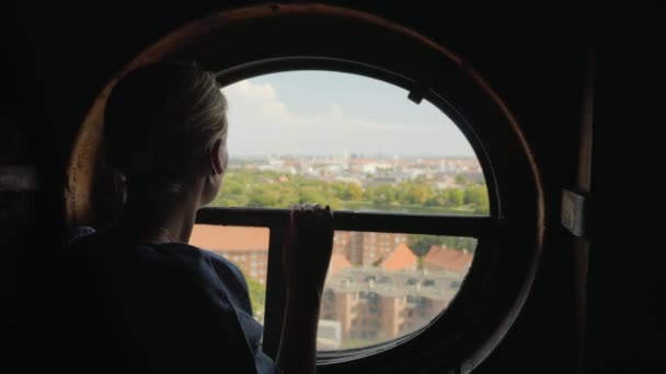Silueta ženy dívající se v kulatém okně na střechách města Kodaně v Dánsku — Stock video