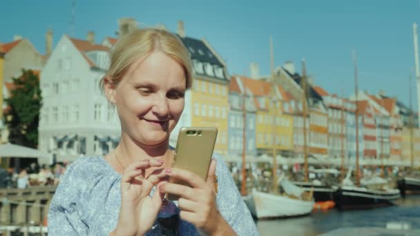 一个快乐的女人用的是智能手机 站在运河的后面 站在哥本哈根的旅游街上 — 图库视频影像