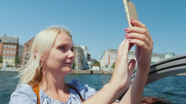 Een vrouw neemt foto's van zichzelf tegen de achtergrond van de stadslijn Copenhagens, zeilen op een sightseeing boot — Stockvideo