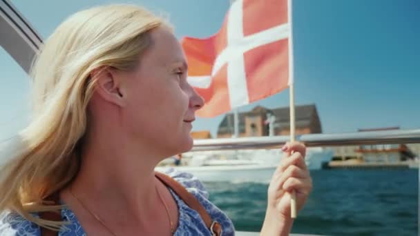 Um turista com a bandeira da Dinamarca navega em um barco de turismo através dos canais da cidade — Vídeo de Stock