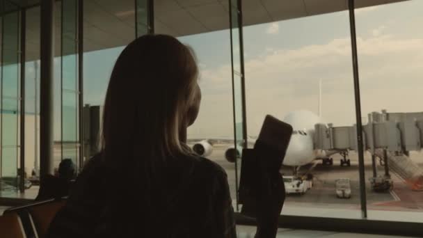 Радісна жінка з документами йде у вікно, де можна побачити великого літака. В очікуванні поїздки — стокове відео