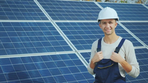 Portrét pracovníka v přilbě, při pohledu na fotoaparát, stojí proti pozadí řádku solárních panelů. Alternativní energie — Stock fotografie