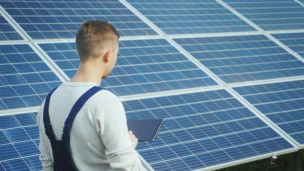 背面: エンジニアは、太陽電池パネルの背景にタブレットを使用しています。代替エネルギー、太陽エネルギー — ストック動画