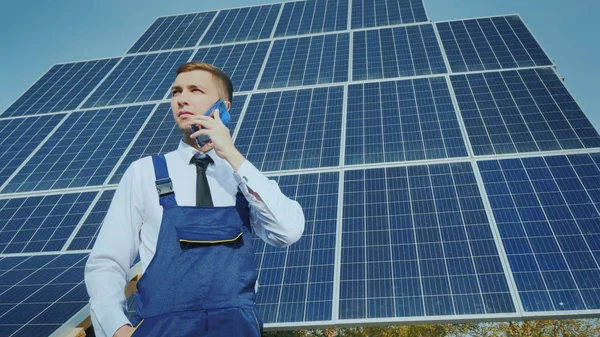 Mladý inženýr mluví po telefonu na pozadí velkých solárních panelů — Stock fotografie